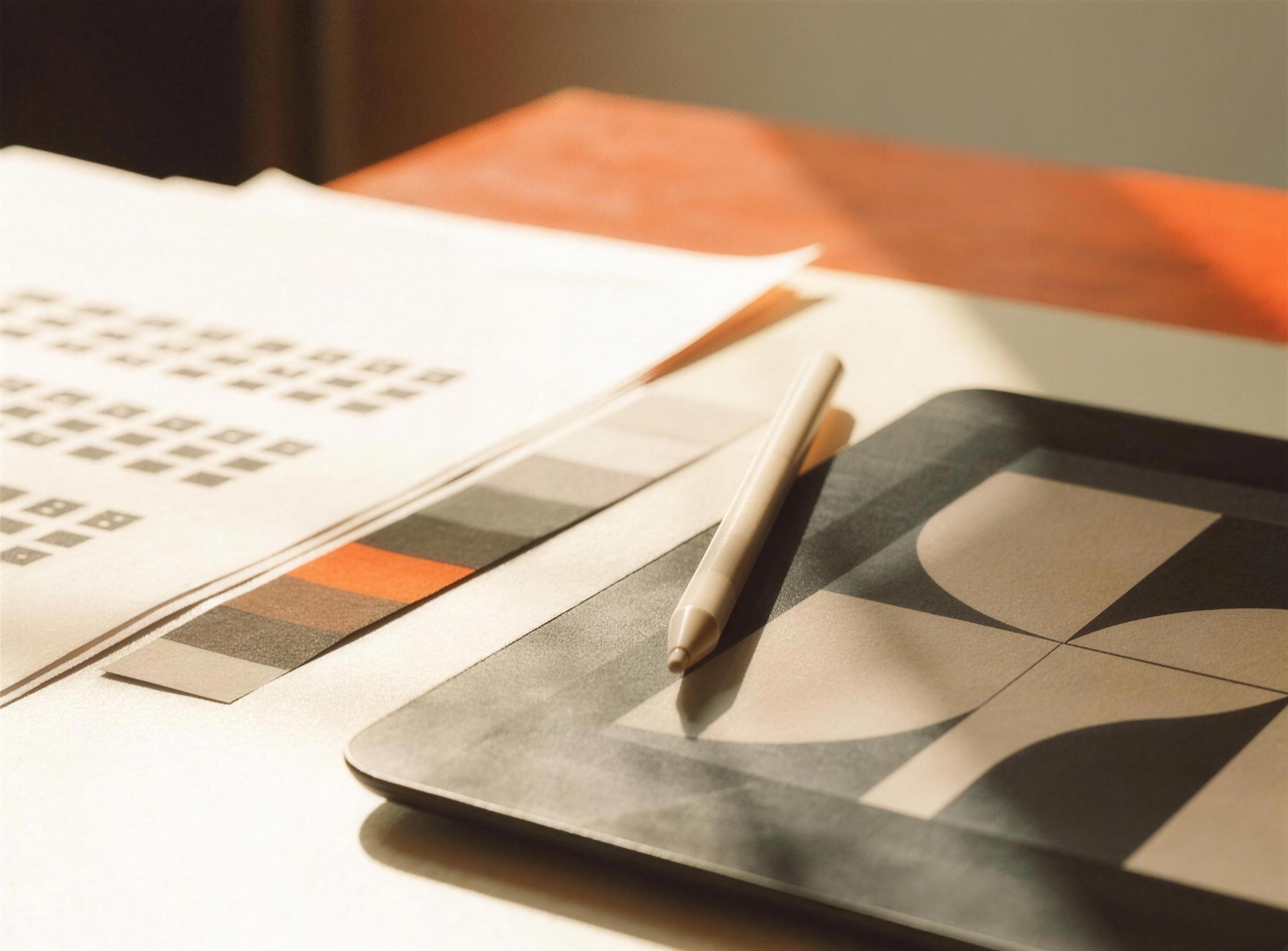 A design desk with type specimens, a color swatch, and geometric work on a tablet
